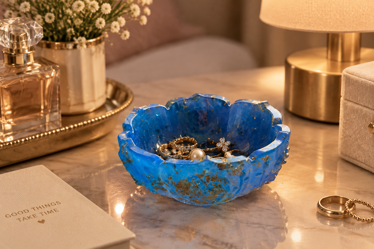 Blue and gold foil resin scalloped trinket bowl holding rings on a marble vanity with lamp light