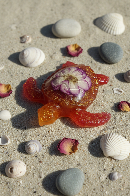Close-up lifestyle shot of orange-red resin sea turtle shell showing purple and white mini rose detail with glitter on sandy surface