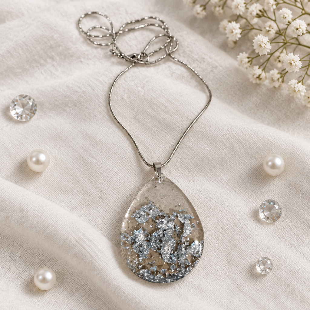 Sparkling silver teardrop pendant necklace shown flat on white linen with pearls and crystals