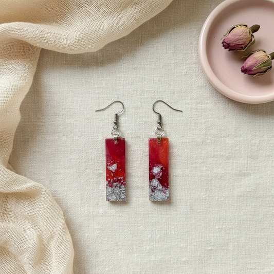 Flat-lay of handmade medium pink and silver foil rectangle resin dangle earrings, composited from the original product photo and styled on cream linen with a dried rose dish and soft fabric