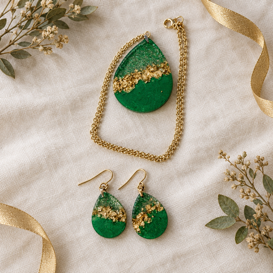 Flat-lay of the emerald and gold foil teardrop pendant necklace and matching earrings styled on neutral linen with greenery and gold ribbon