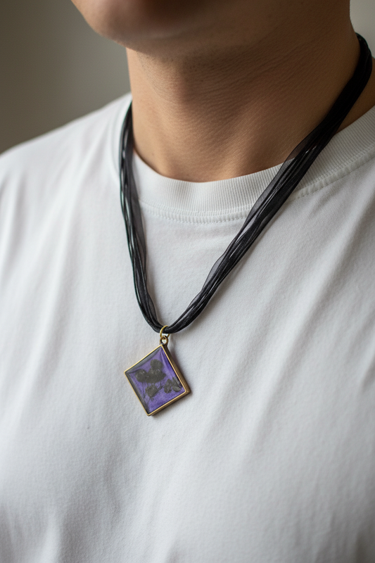 Man wearing handmade purple mica epoxy resin diamond pendant necklace with pressed black gypsophila flowers in gold-tone frame on black organza ribbon, resting against chest over white t-shirt in soft diffused natural light with no glare on pendant