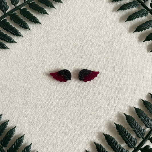 Flat-lay of handmade solid black and burgundy swirled angel wing stud earrings with no inner design, arranged on cream linen