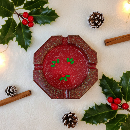 Red glitter octagonal resin ashtray with mistletoe sprinkles shown flat on a white surface with holly and pinecones