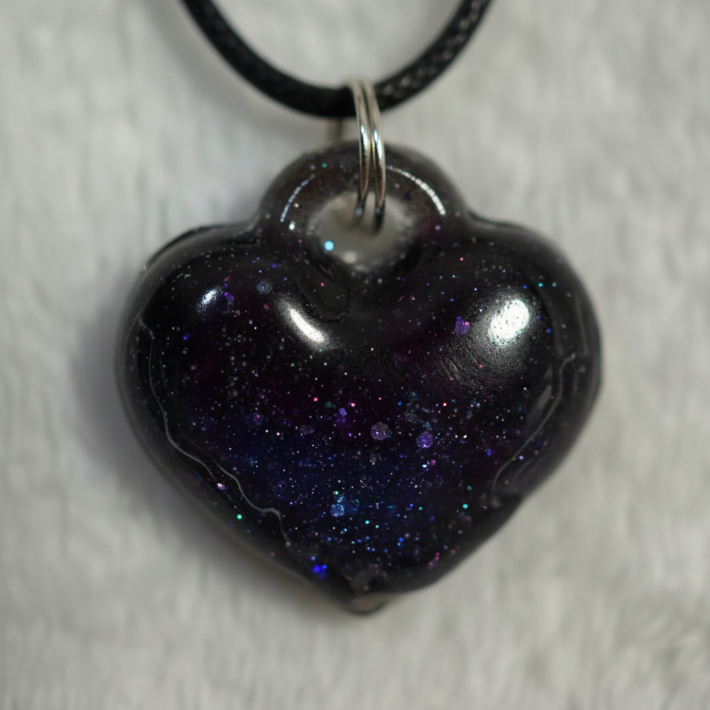 Close-up macro photo of gothic black heart resin pendant with blue and purple glitter shimmer on light background