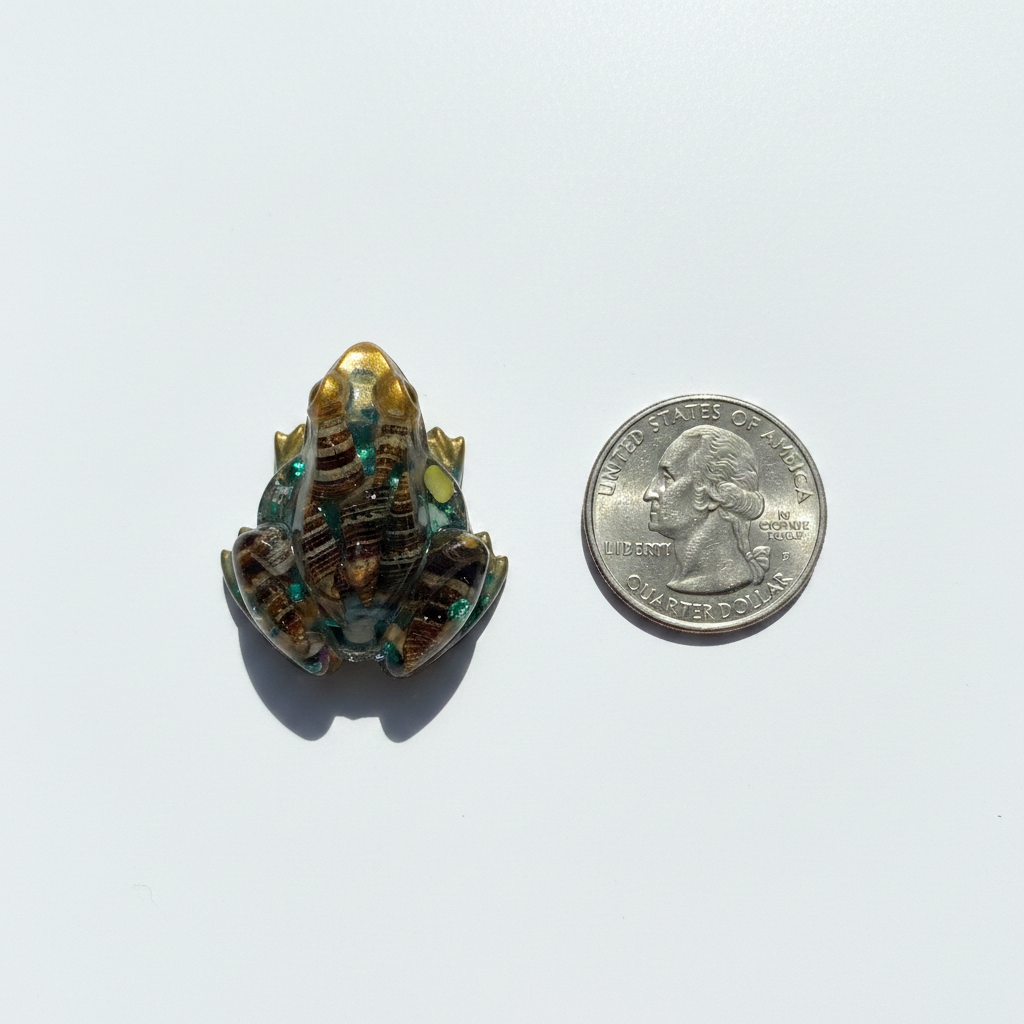 Small amber resin frog figurine with seashells shown next to a US quarter coin for size reference on white surface