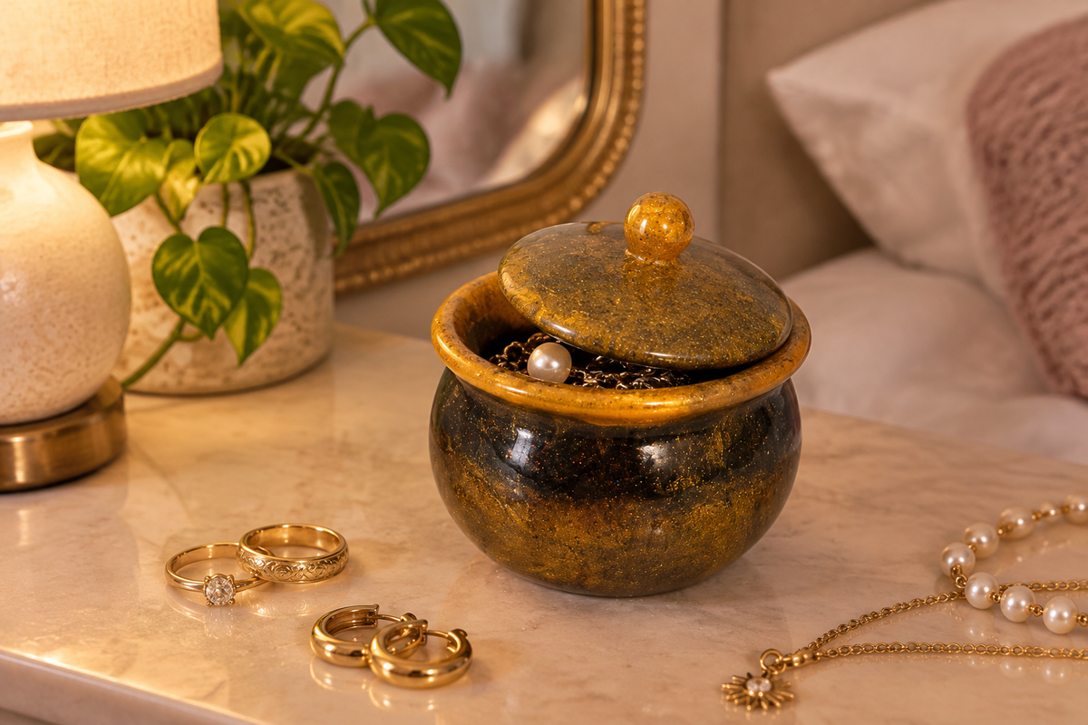 Black and gold cauldron trinket jar with lid ajar on a vanity surrounded by jewelry