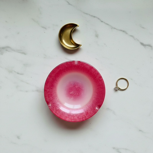 Pink ombré to frosted white round resin ashtray shown flat on a marble surface with a brass crescent moon dish and a ring