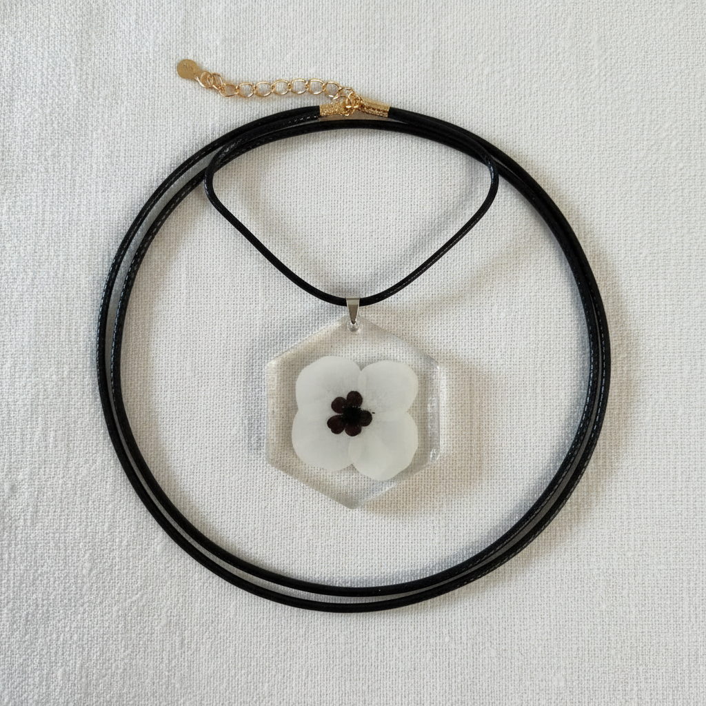White remembrance poppy hexagon pendant necklace with black center shown flat on a white surface
