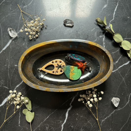 Top-down lifestyle shot of amber and black swirl resin oval decorative bowl with earrings inside on dark slate surface with amber mica rim sparkling