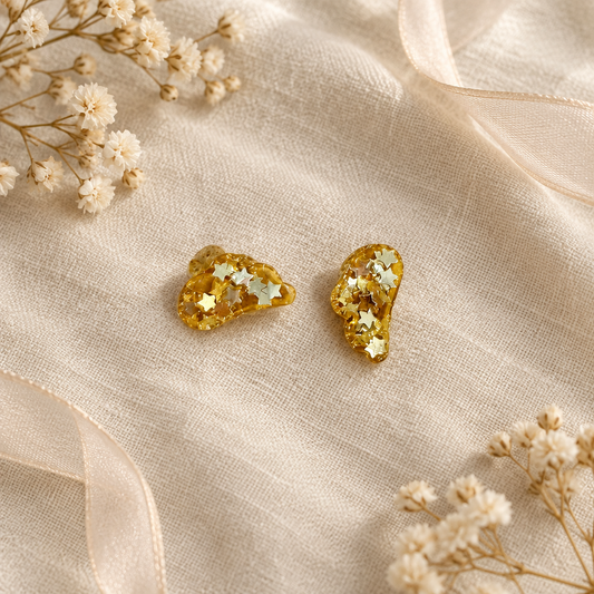 Flat-lay of gold stud earrings on cream linen with dried flowers