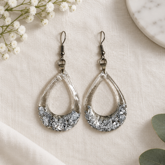 Silver and clear teardrop hoop earrings shown flat on white linen with baby's breath