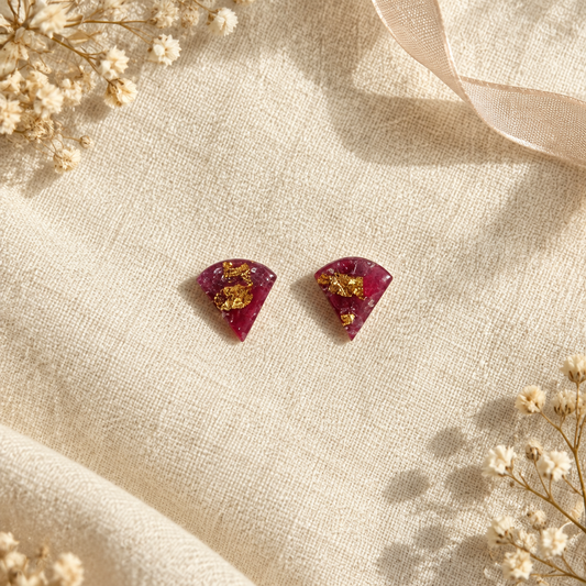 Flat-lay of the burgundy and gold fan stud earrings on cream linen, front view