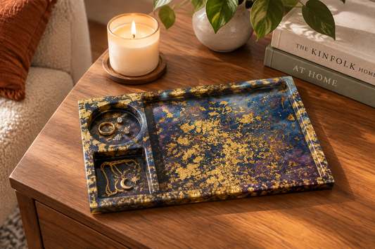 Galaxy dirty pour resin tray with gold foil styled on a wooden side table with jewelry and a candle