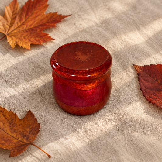 Dark rust resin pudding trinket jar with fitted lid shown flat on linen with autumn leaves